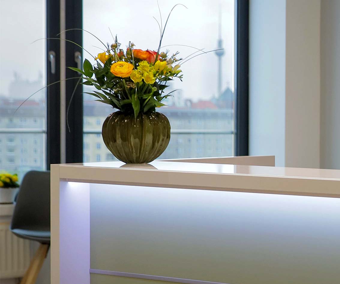 Blick aus dem Empfangsbereich der Praxis mit Blumenstrauß und Berliner Fernsehturm im Hintergrund